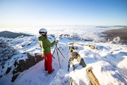 Artist in ski gear paints on a canvas atop a snowy rocky outcropping above the clouds