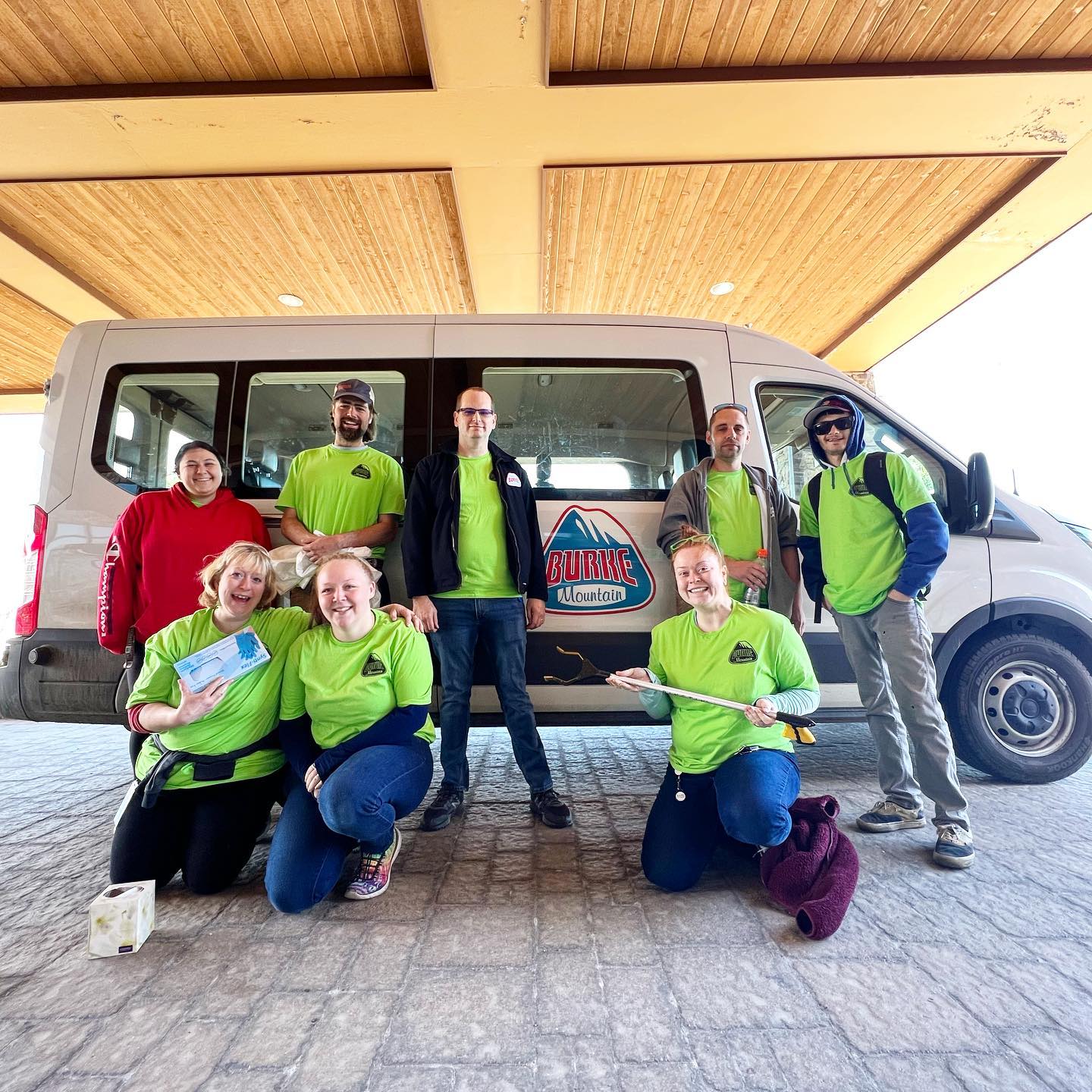 a group of Burke Mountain employees pose in the breezeway of the hotel in front of their Burke branded van after cleaning trash on Green up Day