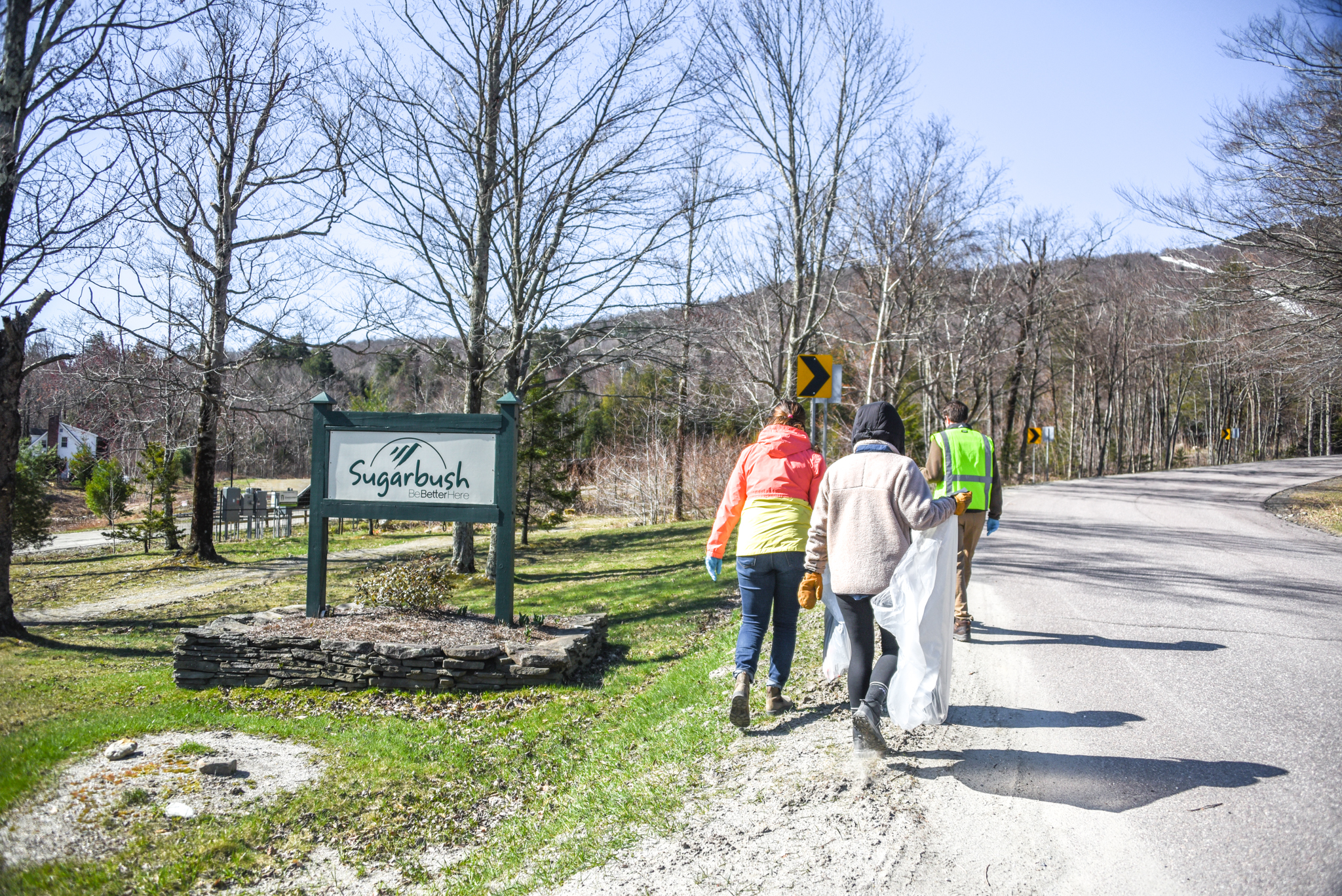 sugarbush employees picking up trash in front of the sugarbush resort sign. photo taken from behind